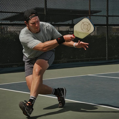A man in athletic wear lunges to strike a pickleball on a court, demonstrating dynamic movement and focus in an outdoor setting.